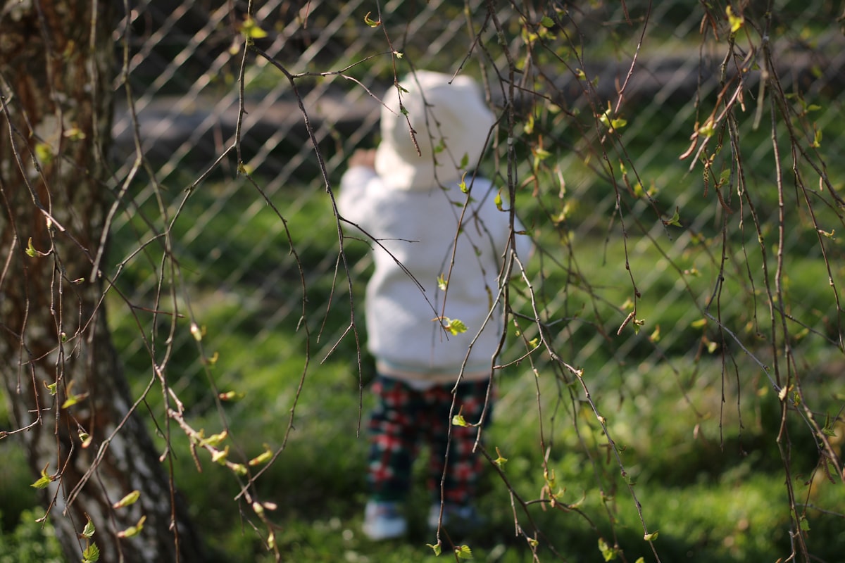 Young child exploring the backyard, crouching down to look at something in the grass on a sunny day