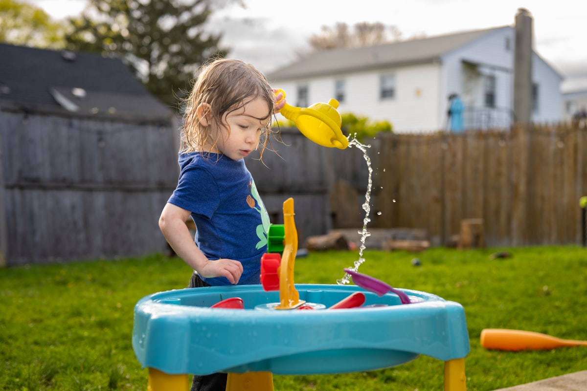 Two toddlers playing together at a brightly colored water table in a sunny backyard