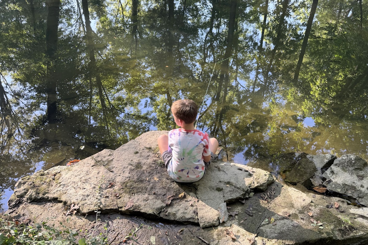 A young toddler playing barefoot outdoors near a creek, exploring rocks and water with curiosity