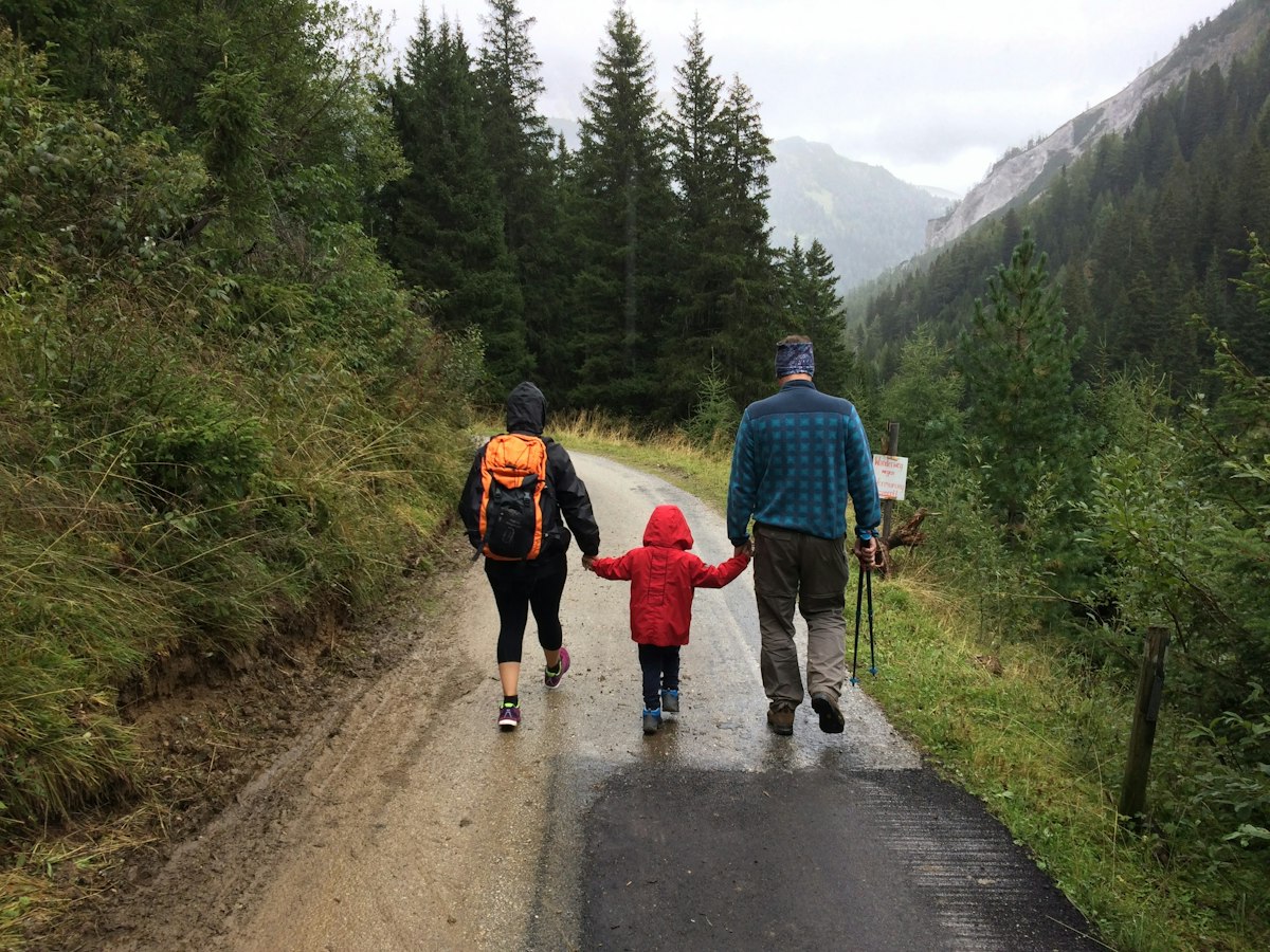 Young child in waterproof hiking boots walking along a muddy forest trail with a parent